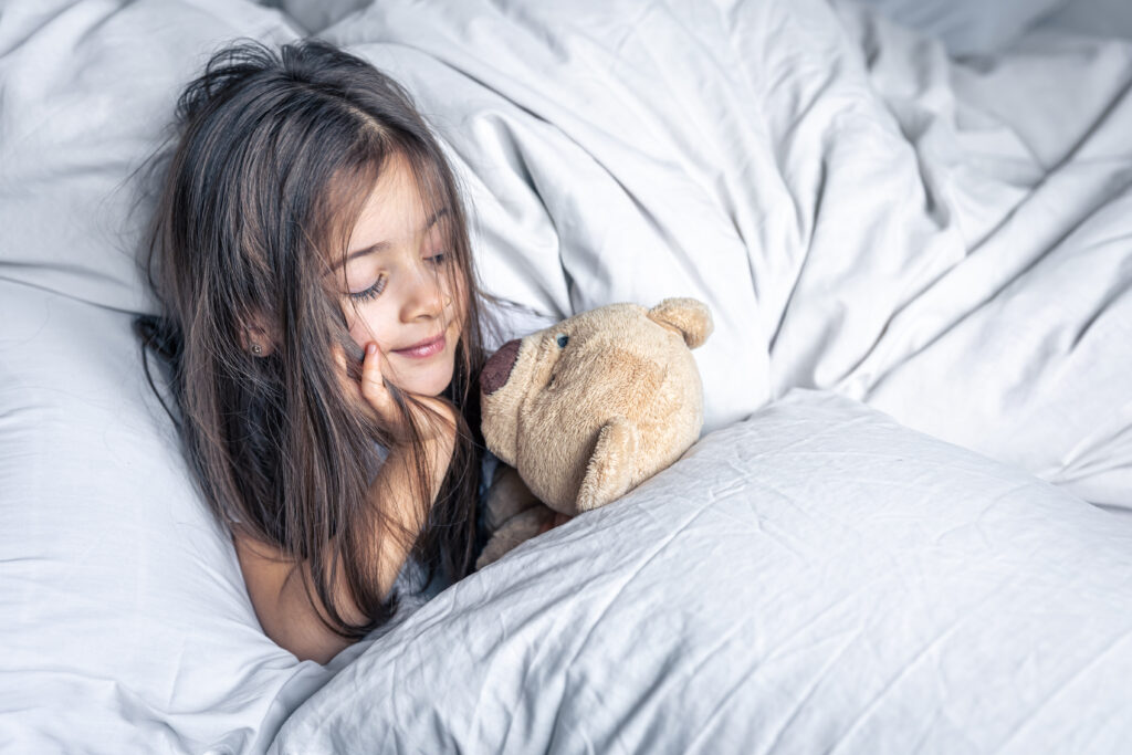 Little cute girl in bed with a teddy bear early in the morning, copy space.